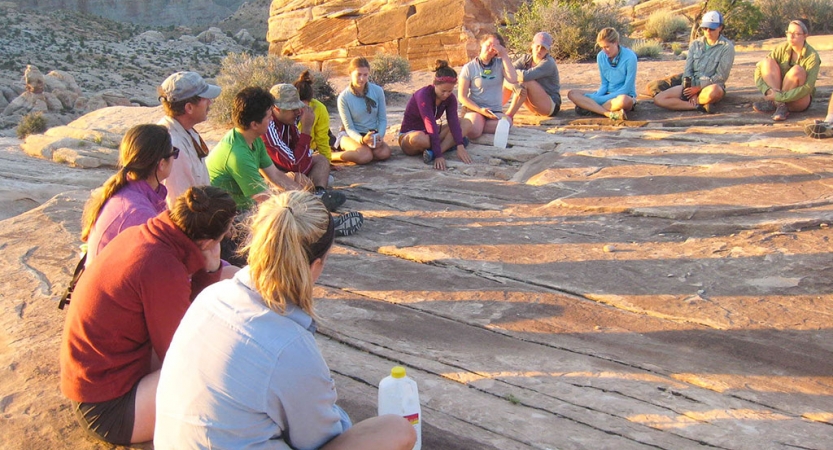A group of people sit in a circle in a desert landscape